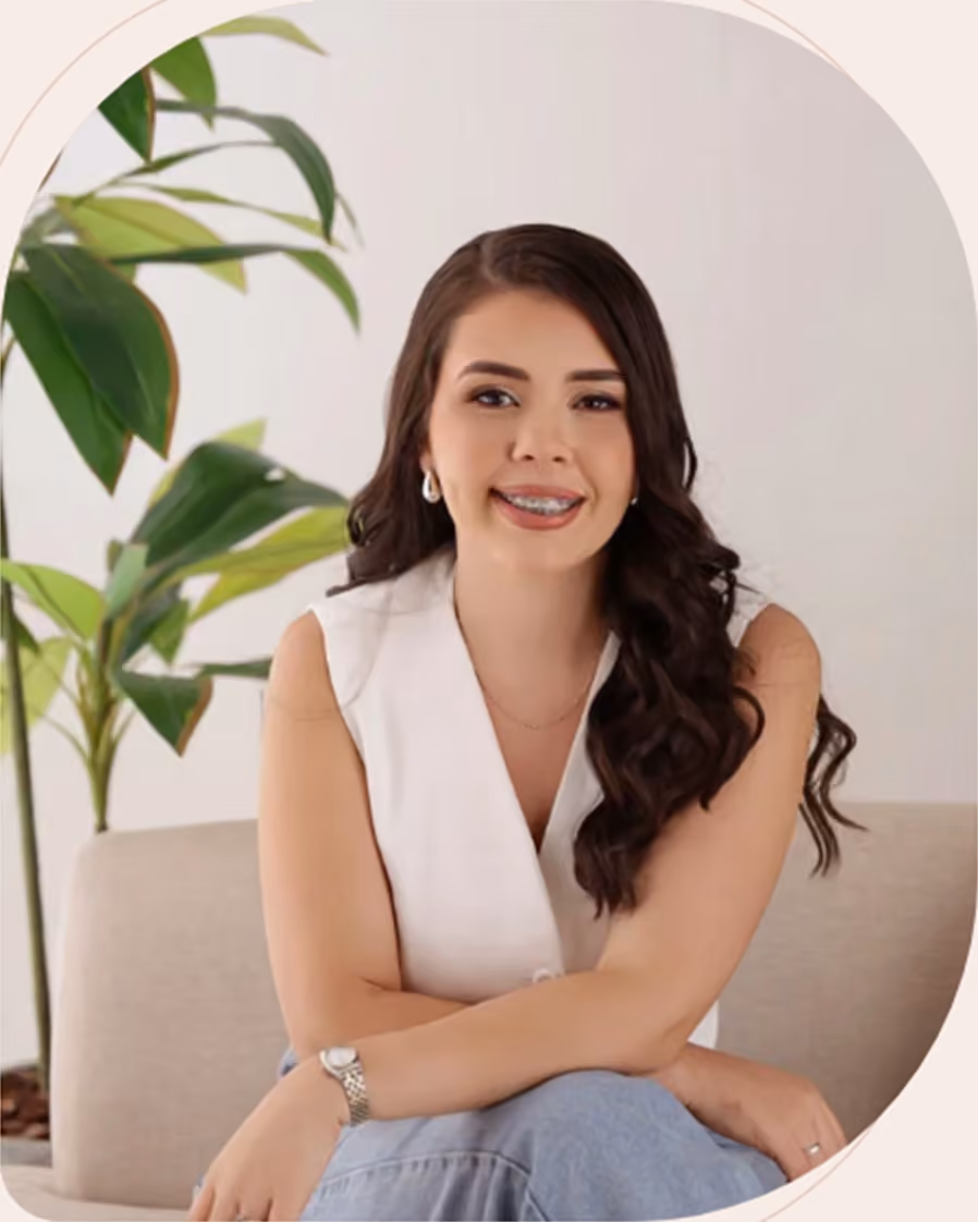 Simone Lima sentada em um sofá claro, ao lado de uma planta